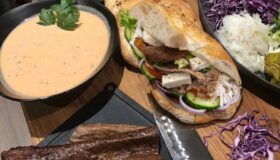 Nahaufnahme eines gedeckten Tisches mit einem Döner-Teller, Salat, verschiedenen Saucen, Fladenbrot und einer halbierten Rotkohlhälfte.