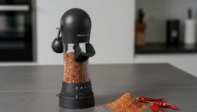 Hochwertige Gewürzmühle von der Kochblume, ideal für die Zubereitung von Speisen in einer Harecker Pfanne. Hier eine Gewürzmühle abgebildet mit einem und gemahlenen und selbst gemachten Döner Gewürz auf einer schwarzen Arbeitsfläche mit ein paar Chili´s daneben.