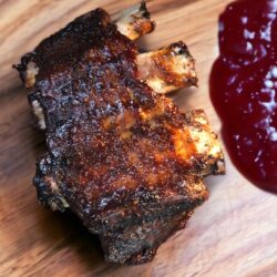 Short Ribs aus dem Ofen, knusprig gebraten mit BBQ Sauce auf einem Holzteller serviert.