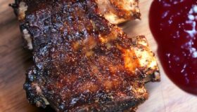 Short Ribs aus dem Ofen, knusprig gebraten mit BBQ Sauce auf einem Holzteller serviert.