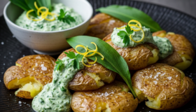 Smashed Potatoes mit Bärlauch-Zitronen-Dip verführisch knusprig auf einem schwarzen Teller angerichtet.