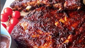 Spareribs auf einem Holzbrett mit Tomaten und BBQ-Sauce angerichtet.