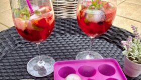 Strawberry-Colada in hohen Gläsern mit frischen Früchten und Eiswürfel mit gefrorenen Früchten, Minze und Basilikum serviert.