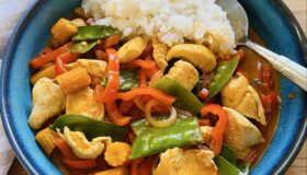 Rotes Thai-Curry mit Hähnchenbrustfilet in einer Schale mit Basmatireis serviert.