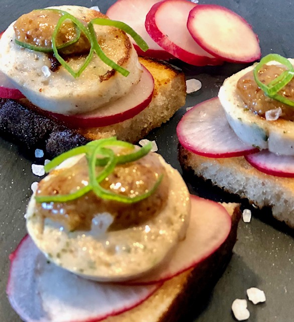 Drei Weißwurst Canapès mit Radieschen und süßen Senf garniert auf einem schwarzen Teller mit Salz angerichtet.