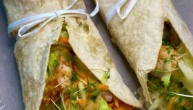 Wrap's mit gebratenen Hähnchenstreifen, Käse und Salat auf einem hellen Teller angerichtet und mit einer Schleife dekoriert.