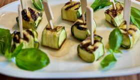 Zucchini-Feta-Päckchen mit Basilikumblättern auf einem weißen Teller angerichtet.
