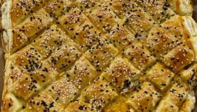Blätterteig Zupfbrot mit gerösteten Auberginen, Kräuterfrischkäse und Cheddar als Füllung. Teig in Rauten geschnitten und mit weißem und dunklem Sesam gebacken. Auf einem Backpapier rustikal serviert.