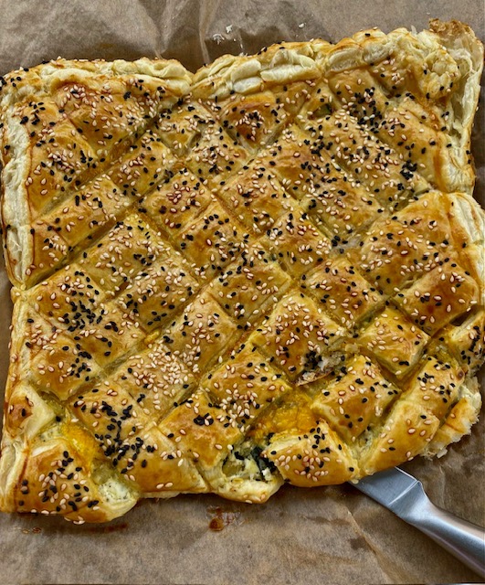 Blätterteig Zupfbrot mit gerösteten Auberginen, Kräuterfrischkäse und Cheddar als Füllung. Teig in Rauten geschnitten und mit weißem und dunklem Sesam gebacken. Auf einem Backpapier rustikal serviert.
