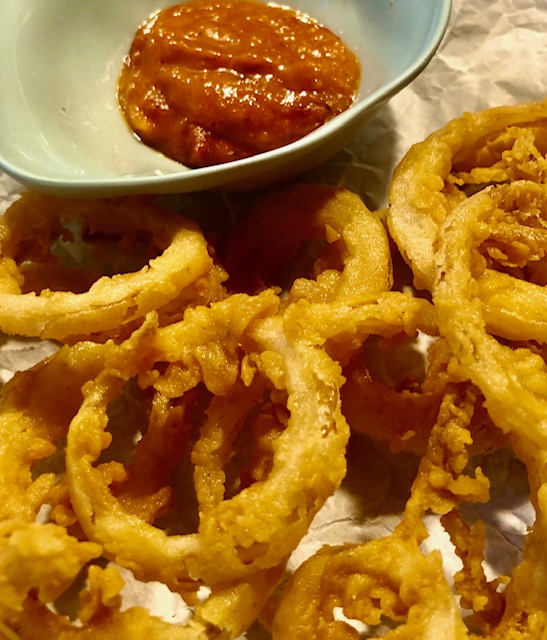Knusprige Zwiebelringe auf einem Teller mit BBQ-Sauce.